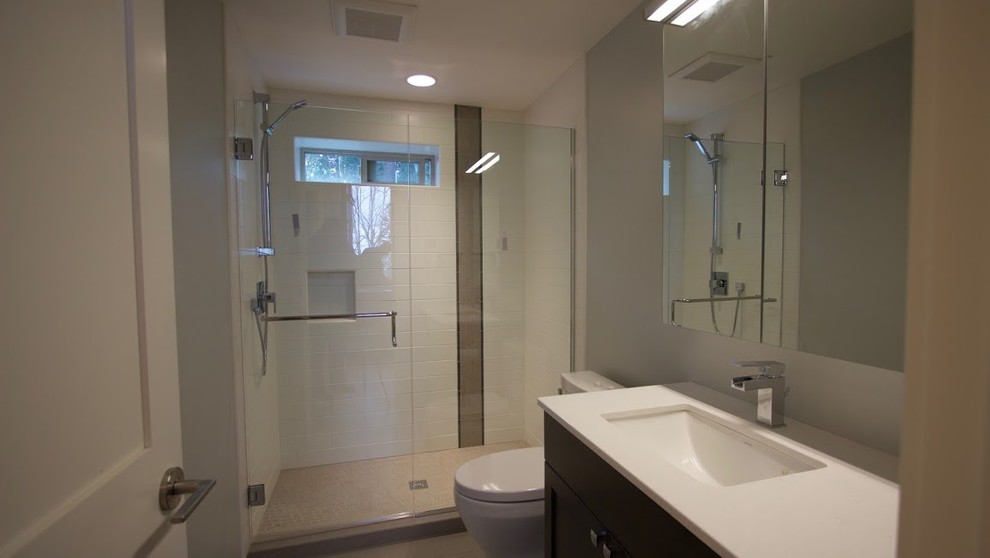 Foto de cuarto de baño principal, actual, de tamaño medio, con armarios con paneles lisos, puertas de armario de madera en tonos medios, ducha a ras de suelo, sanitario de una pieza, lavabo bajoencimera y paredes grises