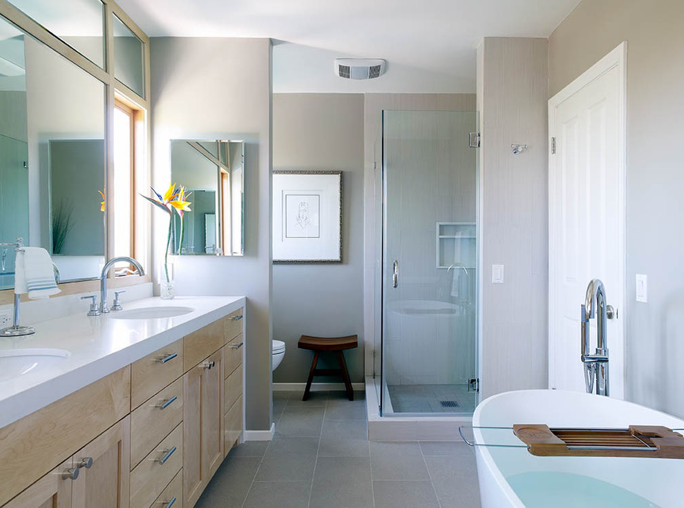 Idéer för ett modernt badrum, med ett undermonterad handfat, skåp i ljust trä, ett fristående badkar, en hörndusch, grå kakel och grått golv