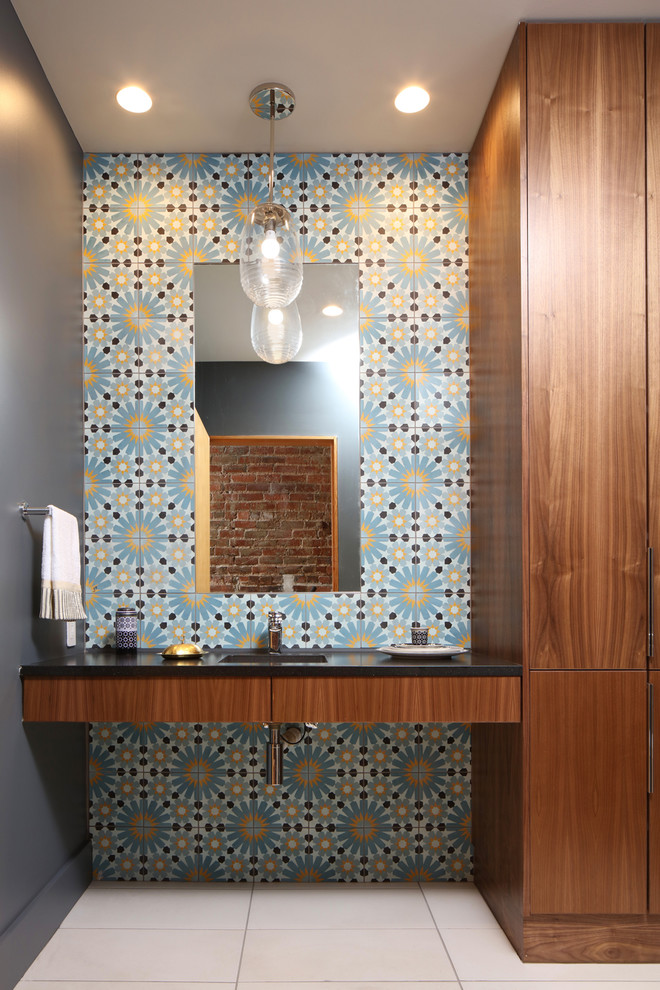 Cette photo montre une salle de bain tendance en bois brun avec un placard à porte plane, un carrelage multicolore, des carreaux de béton, un mur gris, un lavabo encastré, un sol beige et un plan de toilette noir.