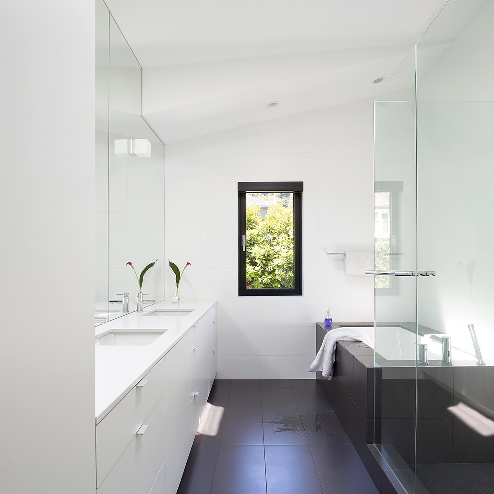 Foto di una stanza da bagno moderna con ante lisce, ante bianche, vasca sottopiano, doccia ad angolo, lavabo sottopiano, pavimento nero e top bianco