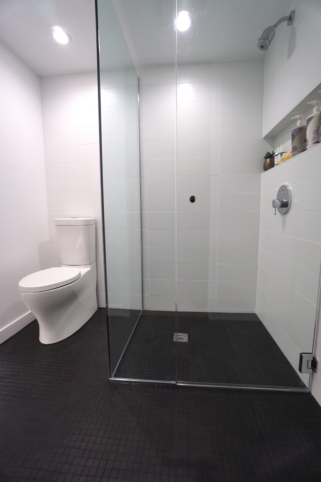 Example of a small minimalist 3/4 black and white tile and ceramic tile ceramic tile walk-in shower design in Seattle with flat-panel cabinets, white cabinets, a two-piece toilet, white walls, an undermount sink and quartz countertops
