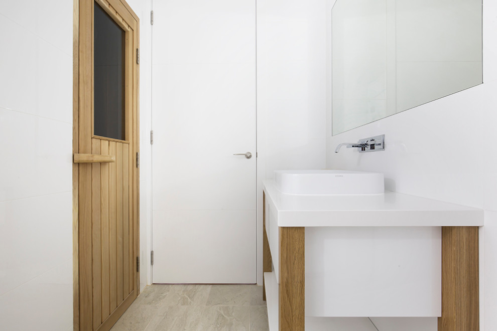 Cette photo montre un petit sauna scandinave en bois clair avec un placard en trompe-l'oeil, une douche d'angle, WC à poser, un carrelage blanc, des carreaux de céramique, un mur blanc, un sol en calcaire, une vasque, un plan de toilette en quartz modifié, un sol beige, une cabine de douche à porte battante, un plan de toilette blanc, meuble simple vasque, meuble-lavabo sur pied et un plafond à caissons.