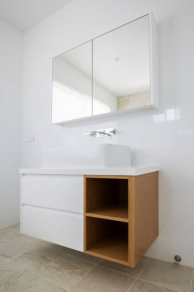 Стильный дизайн: ванная комната среднего размера в скандинавском стиле с фасадами островного типа, светлыми деревянными фасадами, угловым душем, унитазом-моноблоком, белой плиткой, керамической плиткой, белыми стенами, полом из известняка, душевой кабиной, настольной раковиной, столешницей из искусственного кварца, бежевым полом, душем с распашными дверями, белой столешницей, тумбой под одну раковину, подвесной тумбой и кессонным потолком - последний тренд