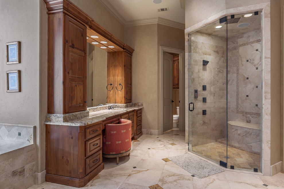 Photo of a large traditional ensuite bathroom in Dallas with raised-panel cabinets, medium wood cabinets, an alcove bath, an alcove shower, a two-piece toilet, beige tiles, marble tiles, beige walls, marble flooring, a submerged sink, granite worktops, beige floors and a hinged door.