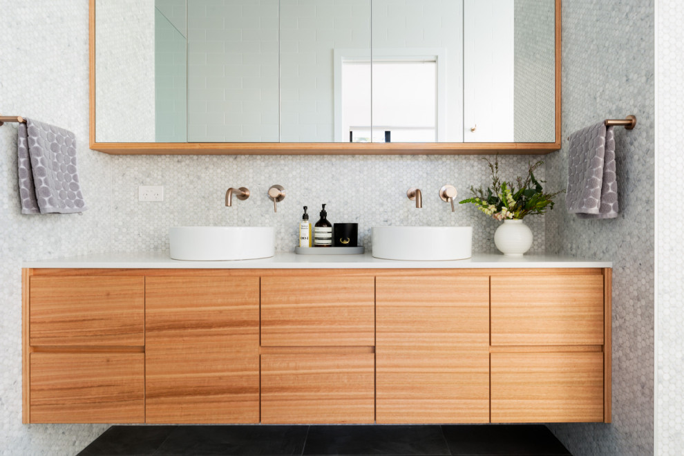 Стильный дизайн: ванная комната в стиле ретро с плоскими фасадами, фасадами цвета дерева среднего тона, серой плиткой, плиткой мозаикой, настольной раковиной, черным полом и белой столешницей - последний тренд