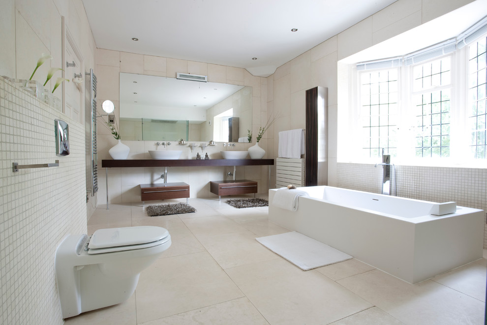 Aménagement d'une salle de bain contemporaine avec une baignoire indépendante, WC suspendus, un carrelage beige, une vasque et un plan de toilette marron.