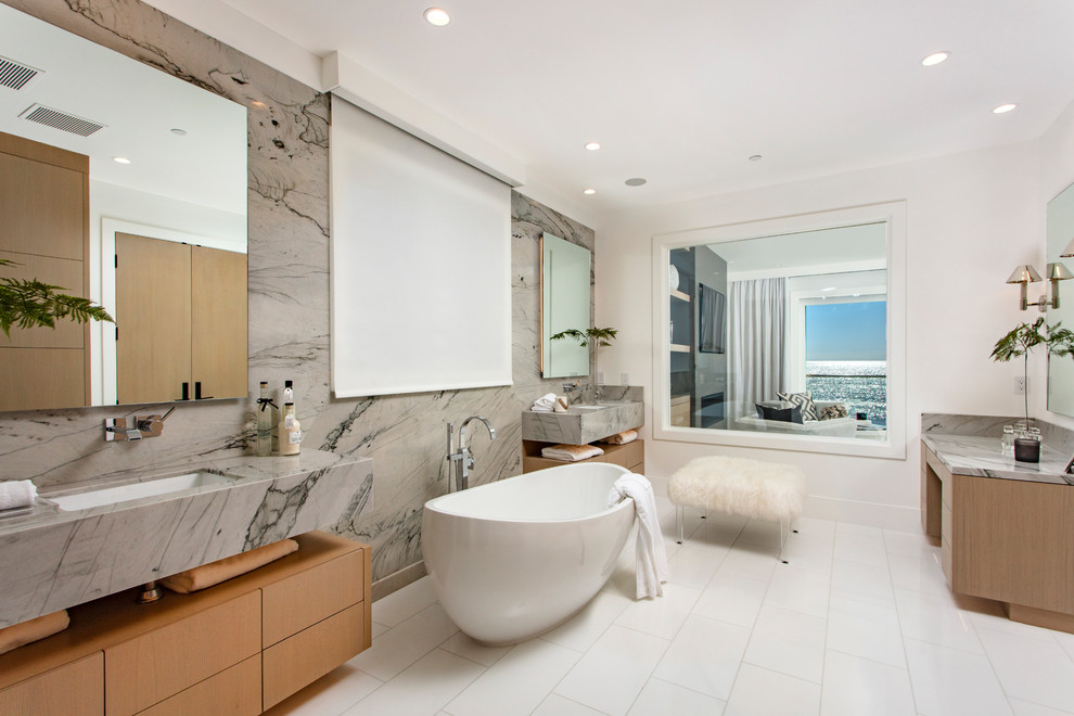 Example of a large beach style master gray tile and marble tile porcelain tile and white floor freestanding bathtub design in Orange County with flat-panel cabinets, brown cabinets, white walls, an undermount sink, marble countertops and gray countertops