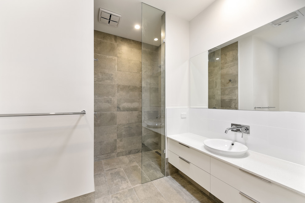 Пример оригинального дизайна: ванная комната среднего размера в стиле модернизм с белыми фасадами, душем в нише, унитазом-моноблоком, белой плиткой, керамогранитной плиткой, белыми стенами, полом из керамогранита, душевой кабиной, накладной раковиной, серым полом, открытым душем и белой столешницей