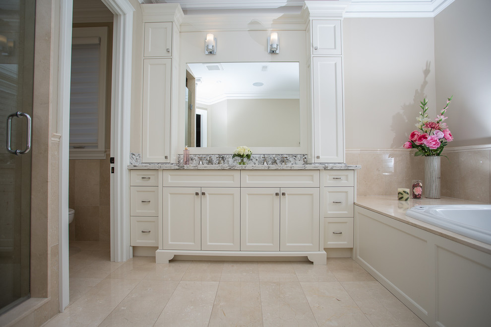Photo of a large traditional ensuite bathroom in Toronto with recessed-panel cabinets, white cabinets, a built-in bath, an alcove shower, a one-piece toilet, grey walls, a submerged sink, beige tiles, ceramic tiles, marble worktops and porcelain flooring.