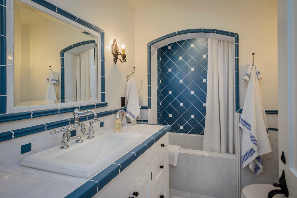 На фото: ванная комната в стиле кантри с накладной раковиной, фасадами с утопленной филенкой, белыми фасадами, столешницей из плитки, синей плиткой, плиткой кабанчик, ванной в нише, душем над ванной и белыми стенами с