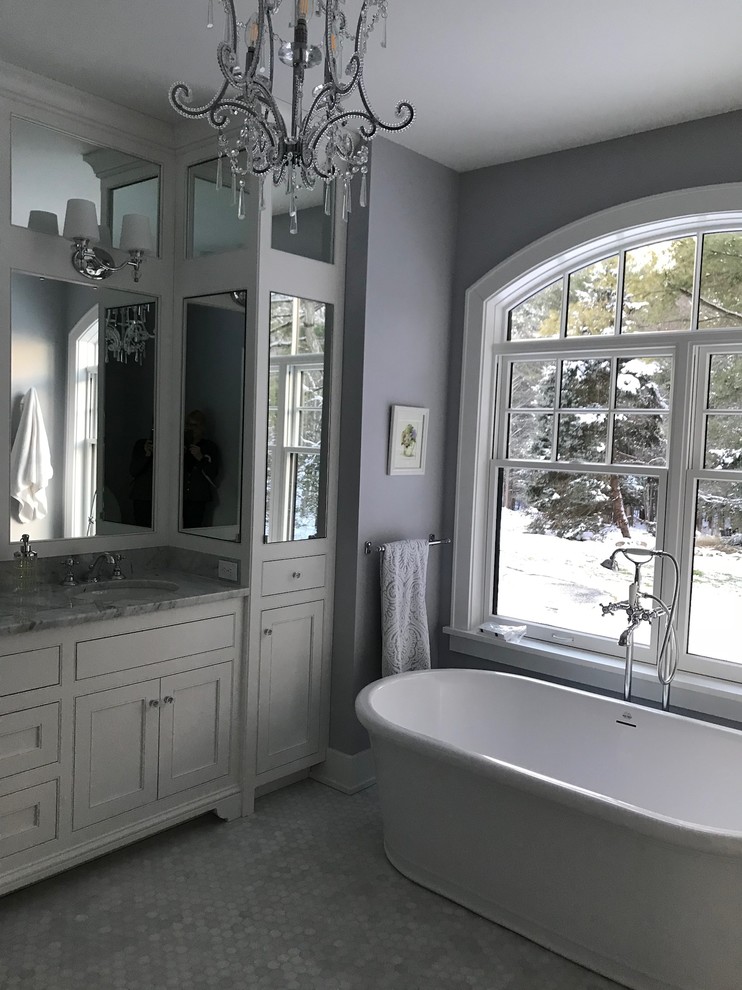 This is an example of a medium sized classic ensuite bathroom in New York with recessed-panel cabinets, white cabinets, a freestanding bath, a corner shower, grey walls, ceramic flooring, a submerged sink, marble worktops, grey floors and a hinged door.