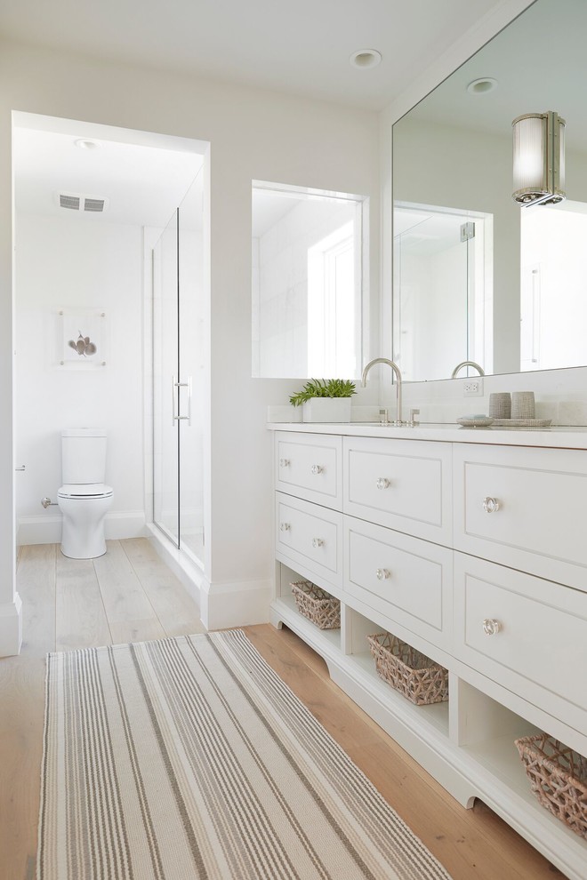 Foto de cuarto de baño costero con puertas de armario blancas, paredes blancas, suelo de madera clara, suelo beige y encimeras blancas