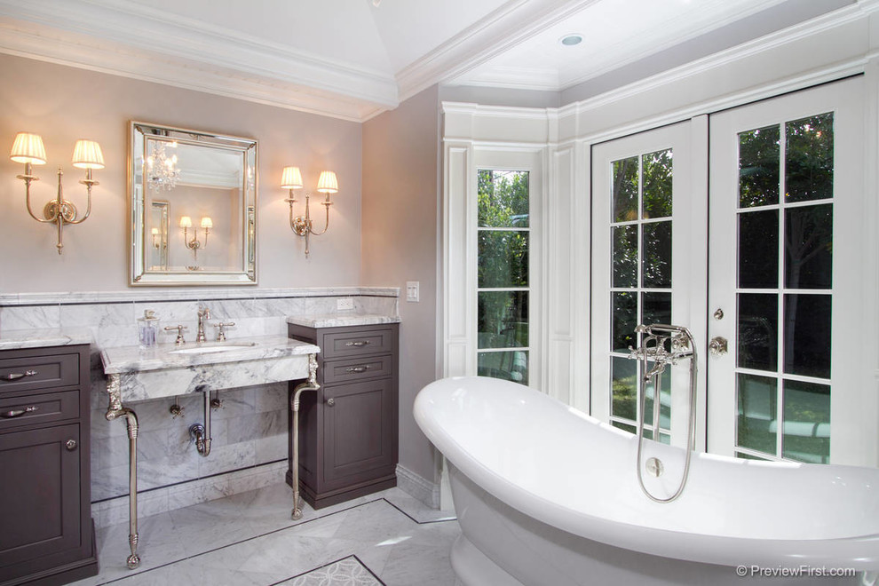 Klassisk inredning av ett badrum, med ett konsol handfat, luckor med infälld panel, skåp i mörkt trä, marmorbänkskiva, ett fristående badkar, en dusch i en alkov, vit kakel och stenkakel