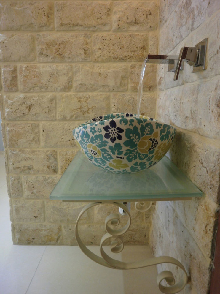 Ispirazione per una stanza da bagno padronale mediterranea con lavabo a bacinella, top in vetro, piastrelle beige, piastrelle in pietra, pavimento con piastrelle in ceramica e pareti beige
