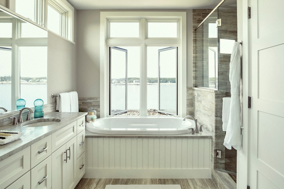 Maritim inredning av ett grå grått badrum, med luckor med infälld panel, vita skåp, ett platsbyggt badkar, grå kakel, grå väggar, ett undermonterad handfat och grått golv
