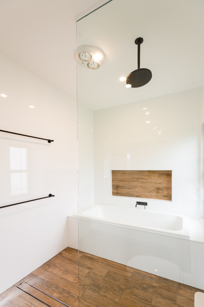 Cette photo montre une salle de bain moderne de taille moyenne avec une baignoire posée, une douche ouverte, un carrelage blanc, un mur blanc et un sol en bois brun.