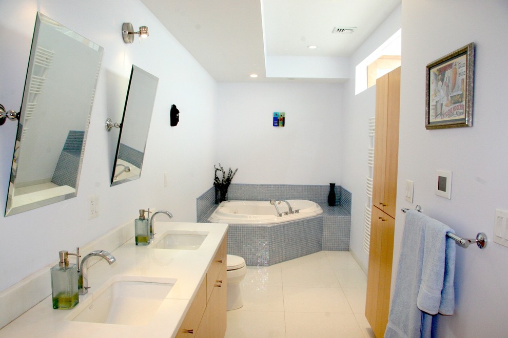 Diseño de cuarto de baño contemporáneo con lavabo bajoencimera, armarios con paneles lisos, puertas de armario de madera clara, encimera de acrílico, jacuzzi, ducha empotrada, sanitario de dos piezas, baldosas y/o azulejos grises y baldosas y/o azulejos de porcelana