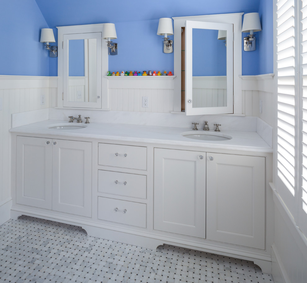 Inredning av ett klassiskt badrum för barn, med luckor med profilerade fronter, vita skåp, en dusch i en alkov, en toalettstol med separat cisternkåpa, svart och vit kakel, mosaik, blå väggar, mellanmörkt trägolv, ett undermonterad handfat och marmorbänkskiva