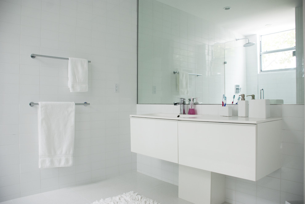 Cette photo montre une grande salle de bain principale moderne avec une douche ouverte, des carreaux de céramique, un mur blanc, un sol en carrelage de céramique, un lavabo intégré, un placard à porte plane, des portes de placard blanches et un plan de toilette en surface solide.