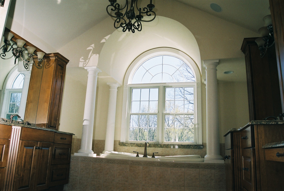Idée de décoration pour une salle de bain principale tradition en bois foncé avec un placard avec porte à panneau surélevé, une baignoire posée, un mur beige, un sol en travertin, un lavabo encastré, un plan de toilette en granite et un sol beige.