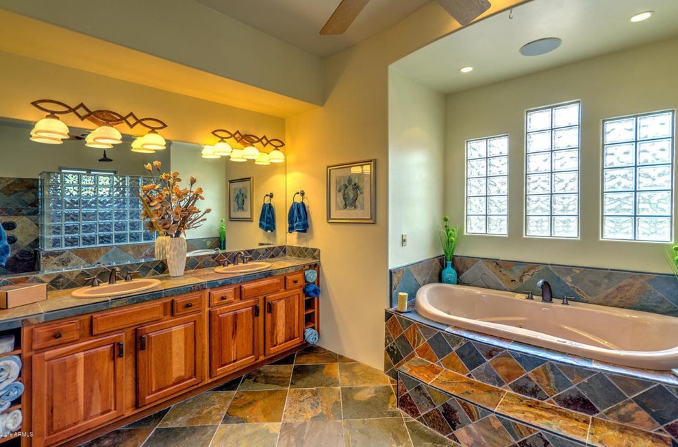 Cette image montre une grande salle de bain principale sud-ouest américain en bois brun avec un placard avec porte à panneau surélevé, un bain bouillonnant, une douche ouverte, WC à poser, un carrelage multicolore, un mur beige, un sol en ardoise et un lavabo posé.