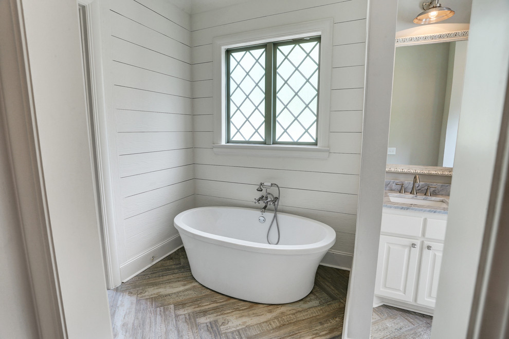 Inredning av ett lantligt grå grått badrum, med luckor med upphöjd panel, vita skåp, ett fristående badkar, grå väggar, marmorgolv, ett undermonterad handfat, marmorbänkskiva och grått golv
