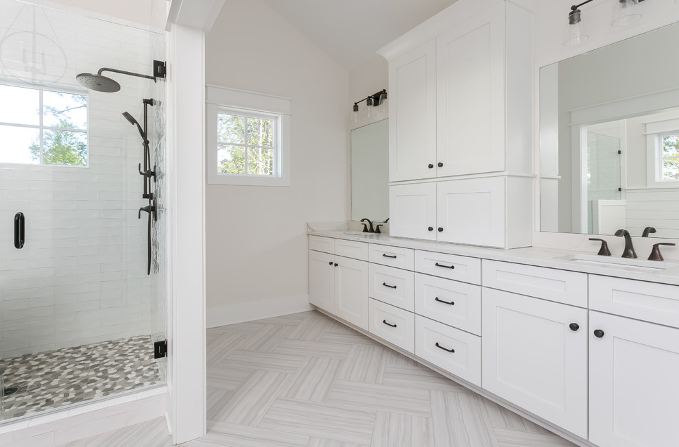 Пример оригинального дизайна: большая главная ванная комната в стиле кантри с плоскими фасадами, белыми фасадами, отдельно стоящей ванной, открытым душем, унитазом-моноблоком, белой плиткой, керамической плиткой, белыми стенами, полом из мозаичной плитки, врезной раковиной, столешницей из искусственного кварца, разноцветным полом, душем с распашными дверями и белой столешницей