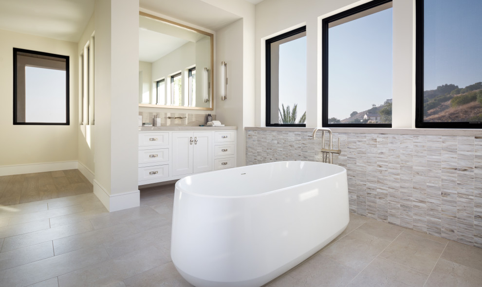 Large minimalist master gray tile, white tile and marble tile porcelain tile and gray floor freestanding bathtub photo in Los Angeles with recessed-panel cabinets, white cabinets, white walls, an undermount sink, limestone countertops and gray countertops