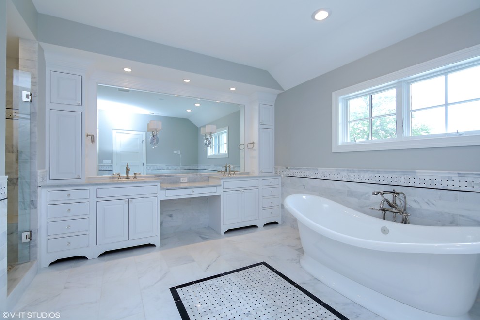 Photo of a large ensuite bathroom in Chicago with raised-panel cabinets, white cabinets, a freestanding bath, a corner shower, grey tiles, ceramic tiles, grey walls, ceramic flooring and a built-in sink.