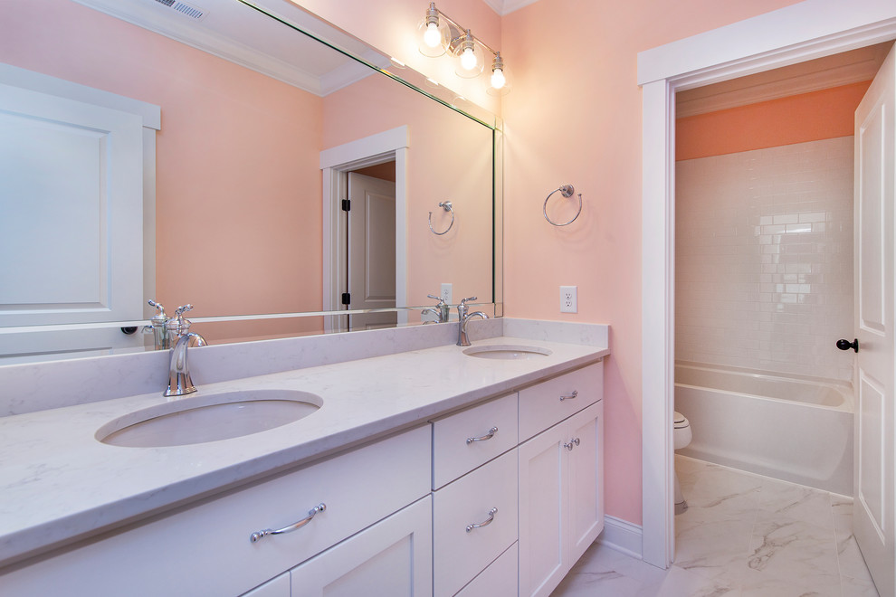 Medium sized traditional ensuite bathroom in Charlotte with recessed-panel cabinets, white cabinets, an alcove bath, a shower/bath combination, a two-piece toilet, white tiles, metro tiles, pink walls, porcelain flooring, a submerged sink, quartz worktops, grey floors, a shower curtain and white worktops.