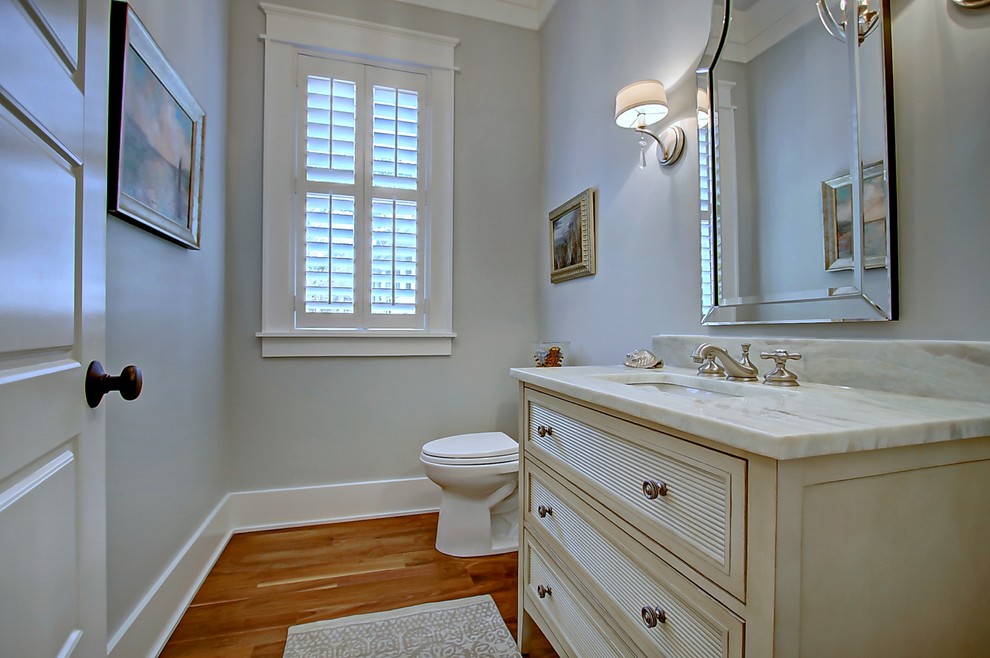 Foto på ett litet vintage badrum, med möbel-liknande, beige skåp, en toalettstol med hel cisternkåpa, grå väggar, mellanmörkt trägolv, ett undermonterad handfat och marmorbänkskiva