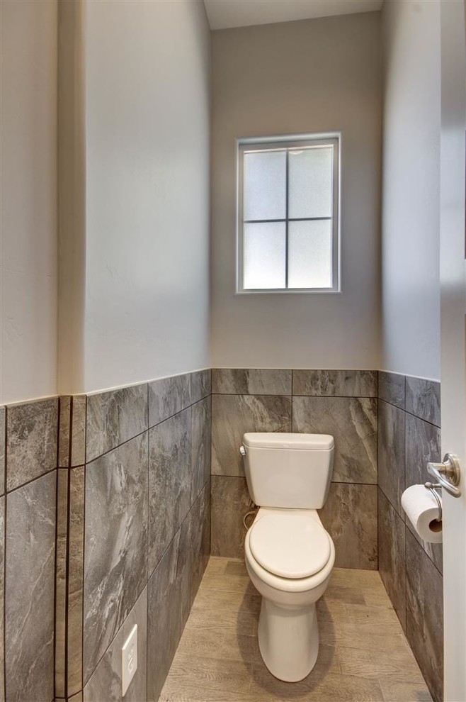 Bild på ett litet amerikanskt toalett, med en toalettstol med hel cisternkåpa, grå väggar och ljust trägolv