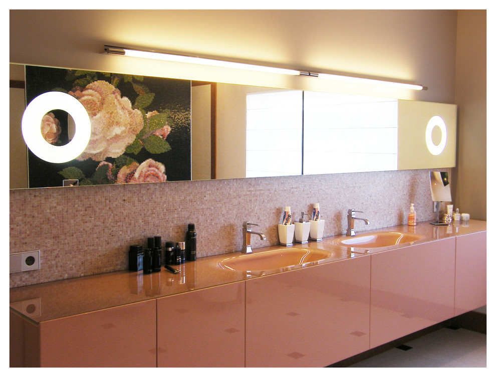 Cette image montre une grande salle de bain principale vintage avec un placard à porte plane, un carrelage rose, mosaïque, un mur beige, un lavabo intégré et un plan de toilette en verre.