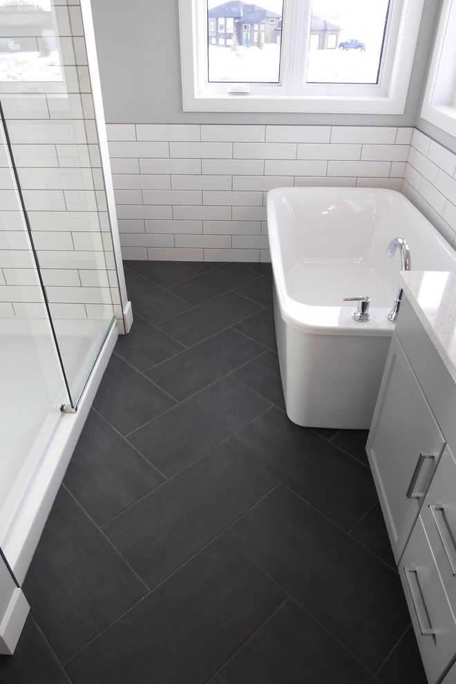 Cette image montre une petite douche en alcôve principale traditionnelle avec un placard à porte shaker, des portes de placard grises, une baignoire indépendante, WC séparés, un carrelage noir, des carreaux de porcelaine, un mur gris, un sol en carrelage de porcelaine, un lavabo encastré et un plan de toilette en quartz.