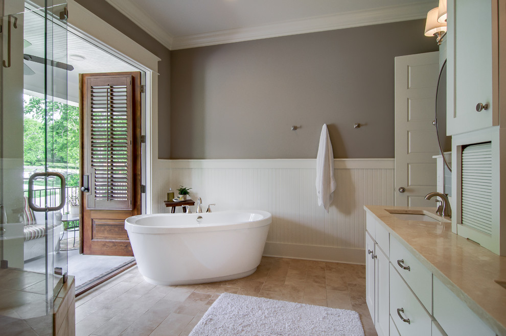 Modelo de cuarto de baño principal clásico con bañera exenta, armarios estilo shaker, puertas de armario beige, baldosas y/o azulejos beige, suelo de piedra caliza y lavabo bajoencimera