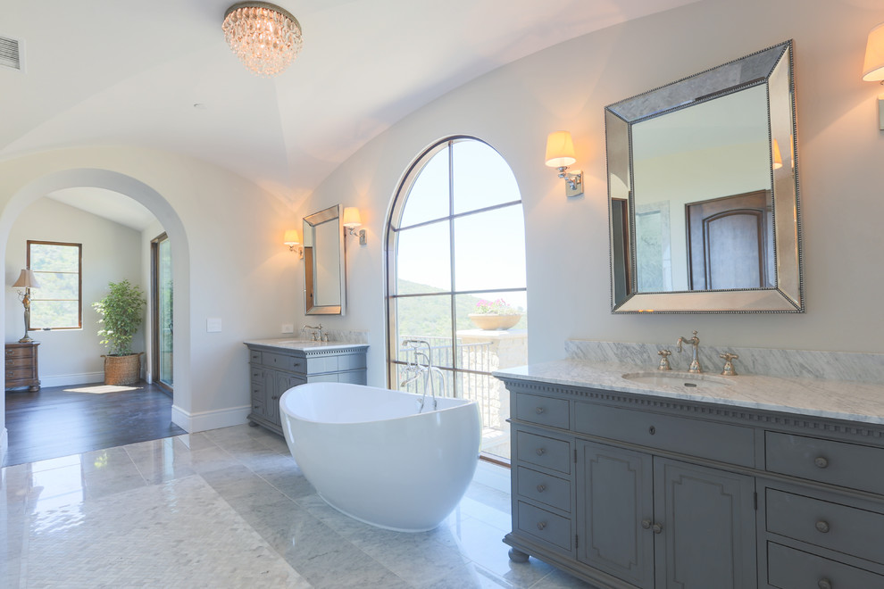 Modelo de cuarto de baño principal mediterráneo grande con armarios con rebordes decorativos, puertas de armario azules, bañera exenta y paredes blancas