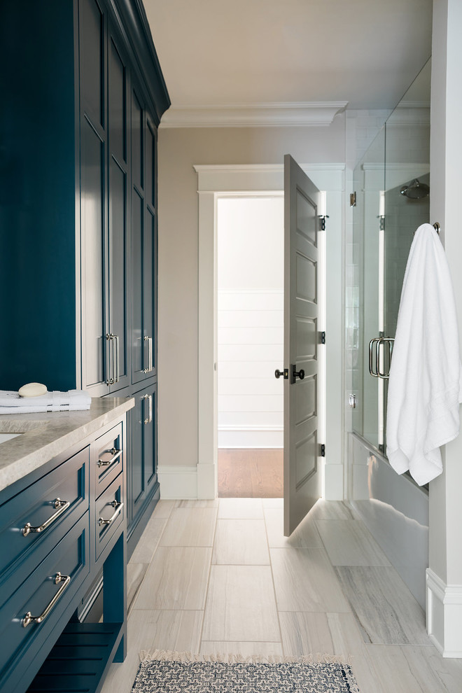 На фото: ванная комната в морском стиле с фасадами с утопленной филенкой, синими фасадами, полновстраиваемой ванной, душем в нише, бежевыми стенами, врезной раковиной, столешницей из гранита, серым полом, душем с распашными дверями и бежевой столешницей