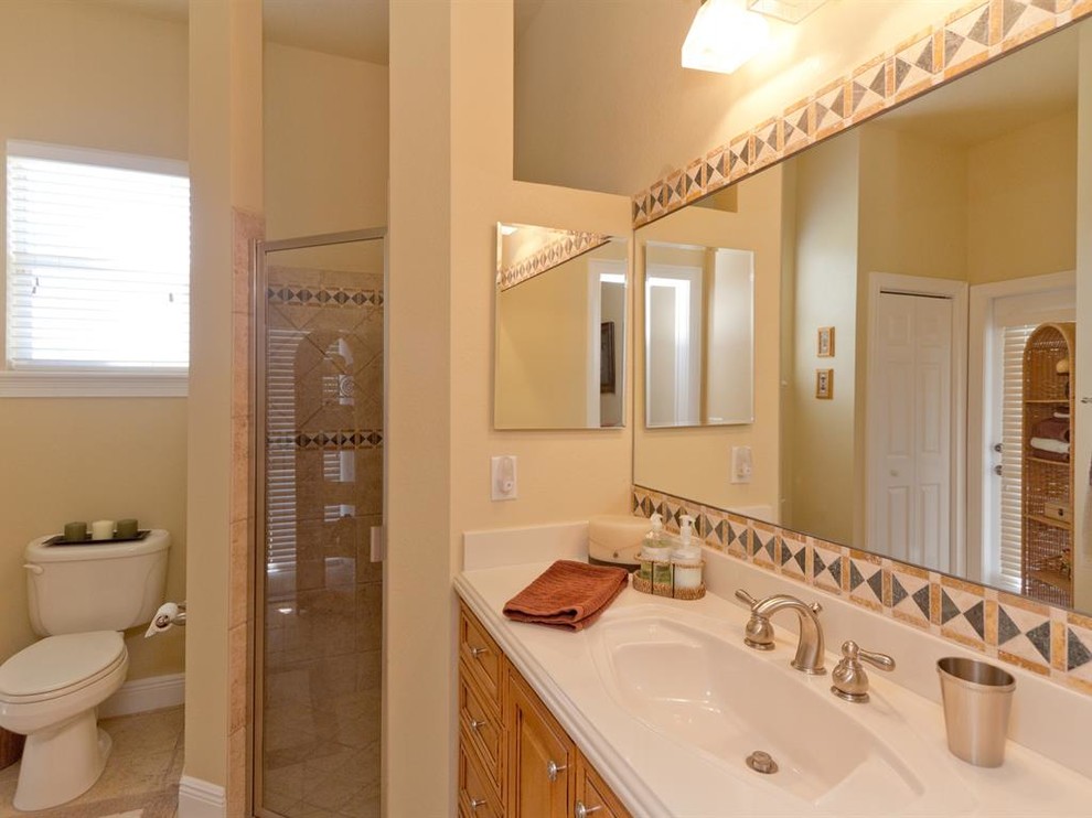 Mid-sized elegant 3/4 beige tile and ceramic tile ceramic tile corner shower photo in Orlando with raised-panel cabinets, medium tone wood cabinets, an integrated sink, solid surface countertops, a one-piece toilet and beige walls