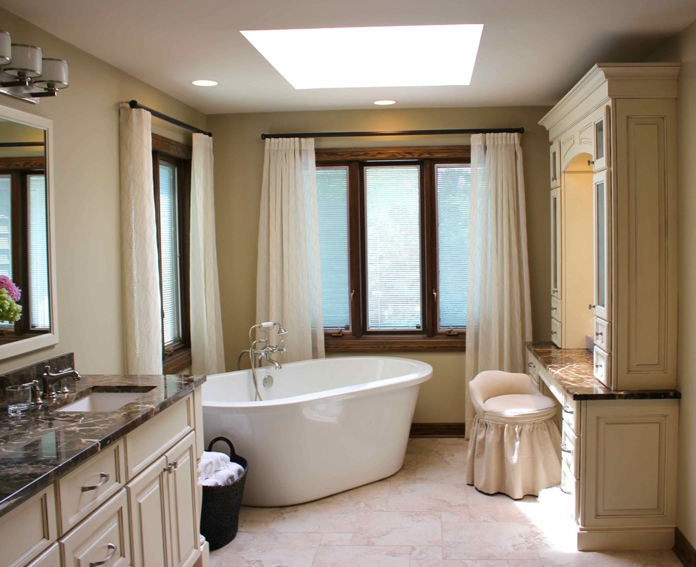 Photo of a large classic ensuite bathroom in Chicago with raised-panel cabinets, beige cabinets, a freestanding bath, a corner shower, a two-piece toilet, beige tiles, porcelain tiles, beige walls, porcelain flooring, a submerged sink, marble worktops, beige floors, a hinged door, brown worktops, double sinks, a built in vanity unit and feature lighting.