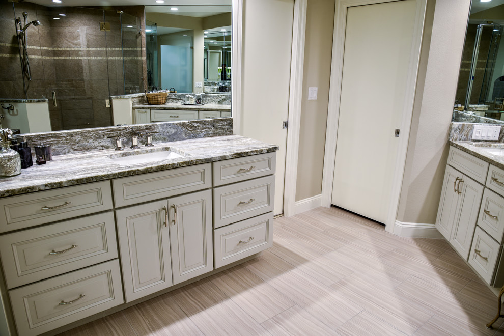 Example of a large transitional master brown tile and porcelain tile porcelain tile and beige floor bathroom design in Tampa with raised-panel cabinets, white cabinets, beige walls, a drop-in sink, granite countertops and a hinged shower door