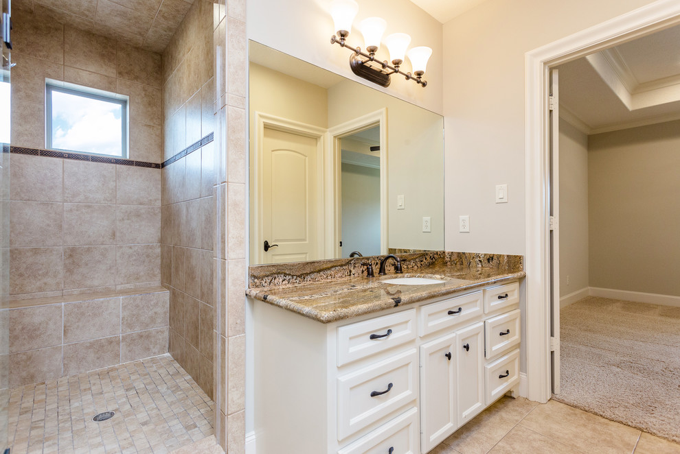 Large mediterranean bathroom in Houston with recessed-panel cabinets, white cabinets, a two-piece toilet, beige tiles, travertine tiles, beige walls, travertine flooring, a submerged sink, granite worktops, beige floors, brown worktops, a built-in shower and an open shower.