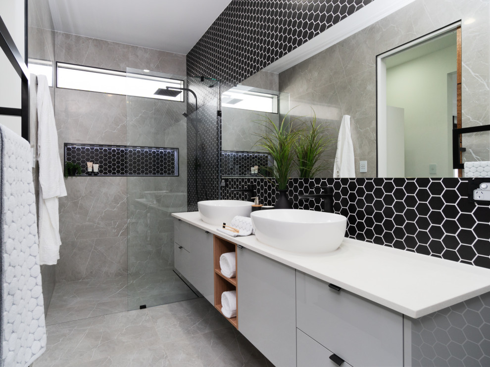 Стильный дизайн: большая ванная комната в современном стиле с плоскими фасадами, серыми фасадами, душем в нише, черной плиткой, серой плиткой, душевой кабиной, настольной раковиной, серым полом, открытым душем, белой столешницей, нишей, тумбой под две раковины и подвесной тумбой - последний тренд
