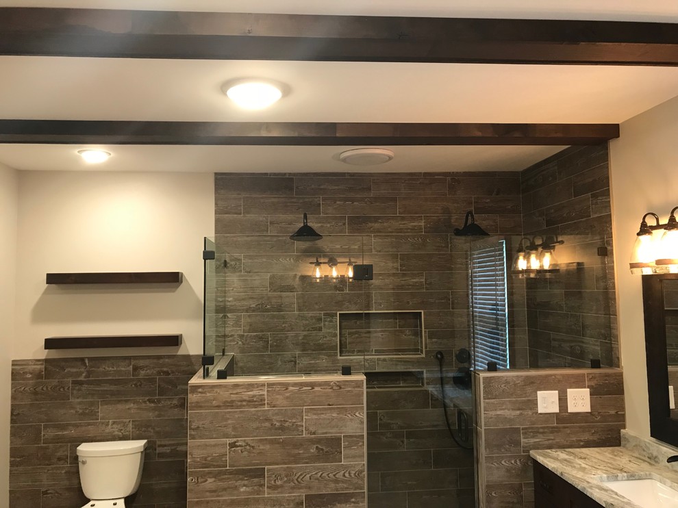 This is an example of a medium sized rustic ensuite bathroom in Nashville with a corner shower, a one-piece toilet, brown tiles, porcelain tiles, beige walls, limestone flooring, a submerged sink, granite worktops, beige floors, a hinged door, dark wood cabinets, grey worktops and shaker cabinets.