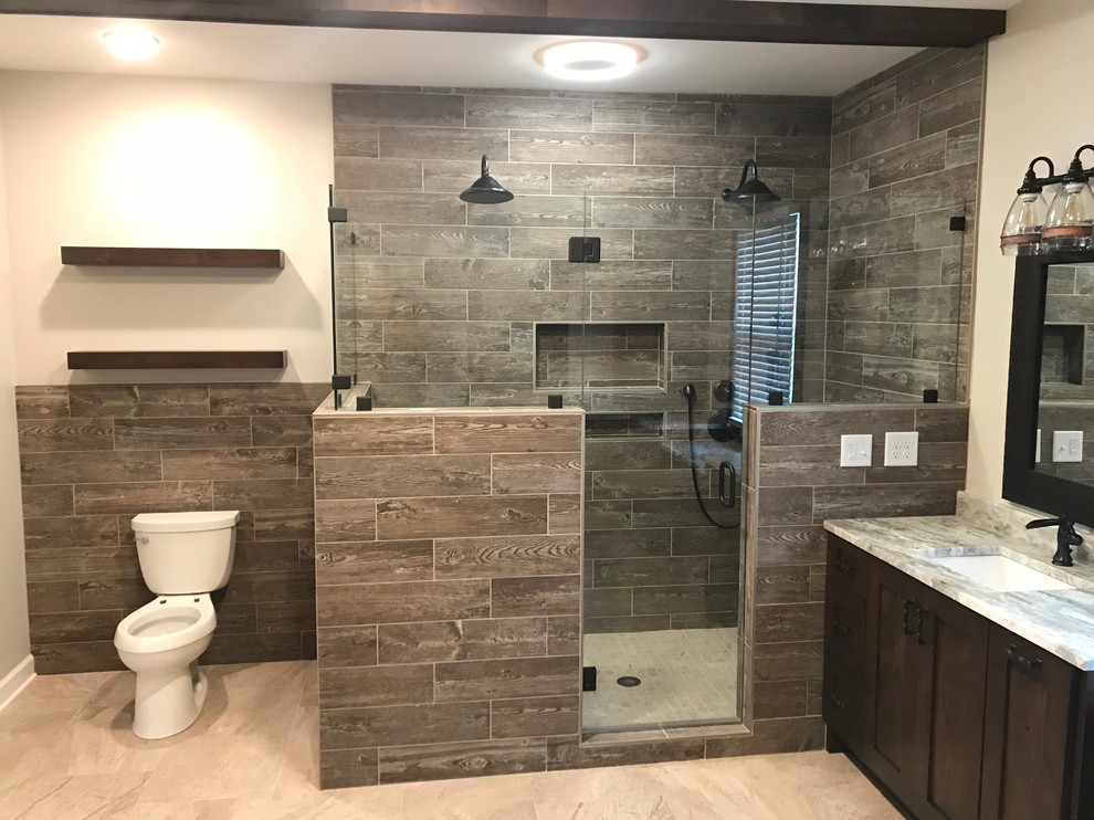 This is an example of a medium sized rustic ensuite bathroom in Nashville with a corner shower, a one-piece toilet, brown tiles, porcelain tiles, beige walls, limestone flooring, beige floors, a hinged door, shaker cabinets, dark wood cabinets, a submerged sink, granite worktops and grey worktops.