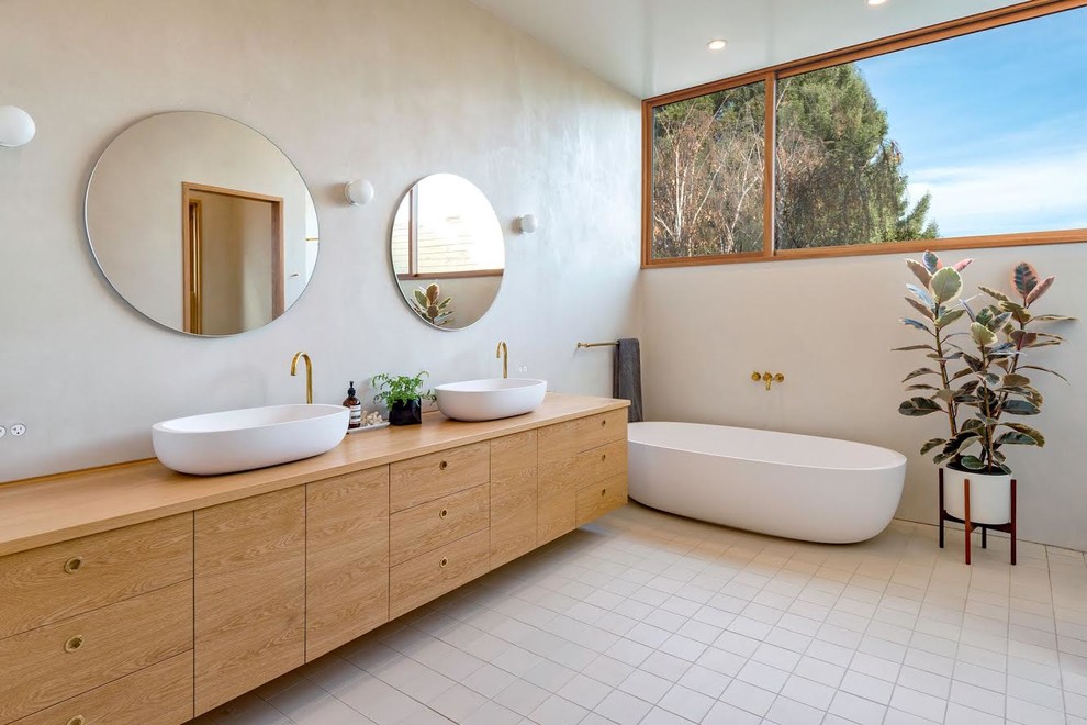 Photo of a scandinavian ensuite bathroom in San Francisco with flat-panel cabinets, light wood cabinets, a freestanding bath, beige walls, a vessel sink, wooden worktops, beige floors and beige worktops.