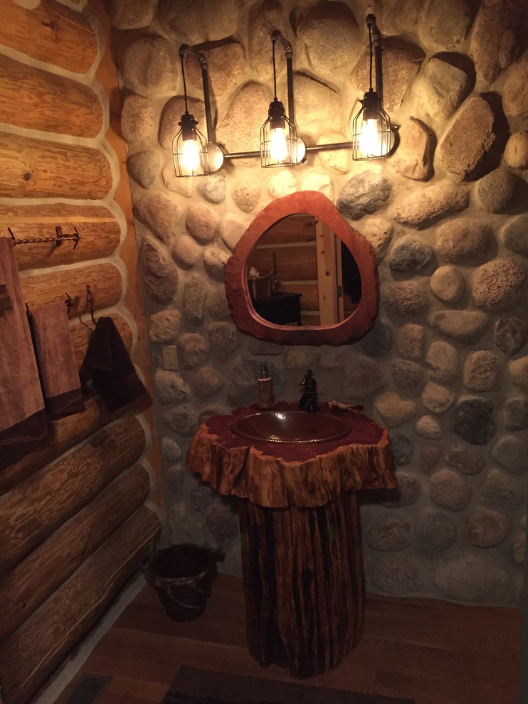 Ejemplo de cuarto de baño rústico con lavabo con pedestal, puertas de armario de madera oscura, encimera de madera, baldosas y/o azulejos de piedra y suelo de madera en tonos medios