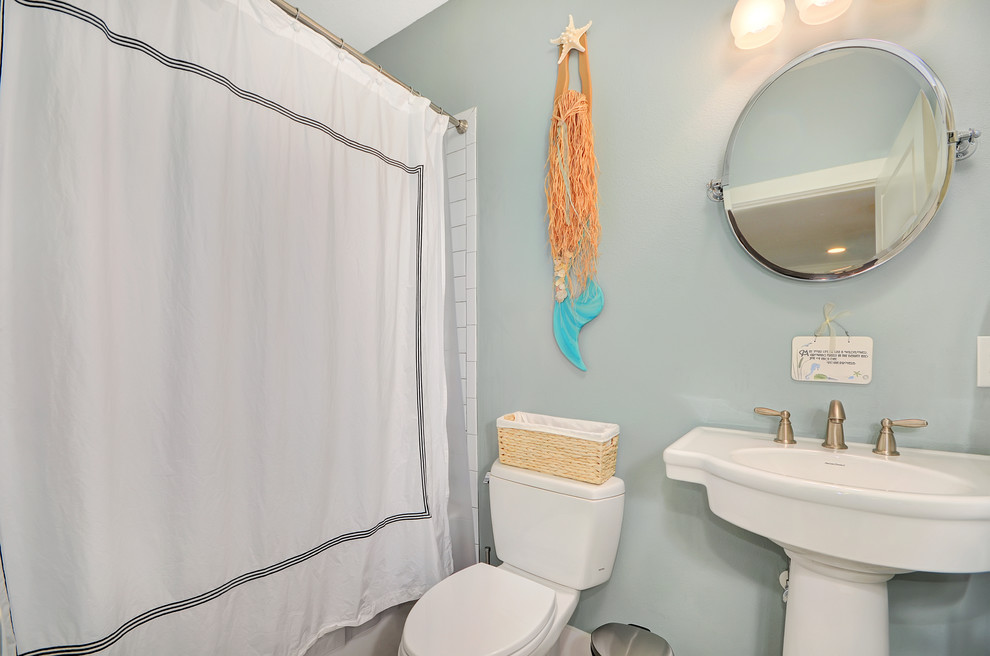 Modelo de cuarto de baño de estilo americano pequeño con bañera empotrada, ducha empotrada, sanitario de dos piezas, baldosas y/o azulejos blancos, baldosas y/o azulejos de cemento, paredes azules, aseo y ducha, lavabo con pedestal y ducha con cortina