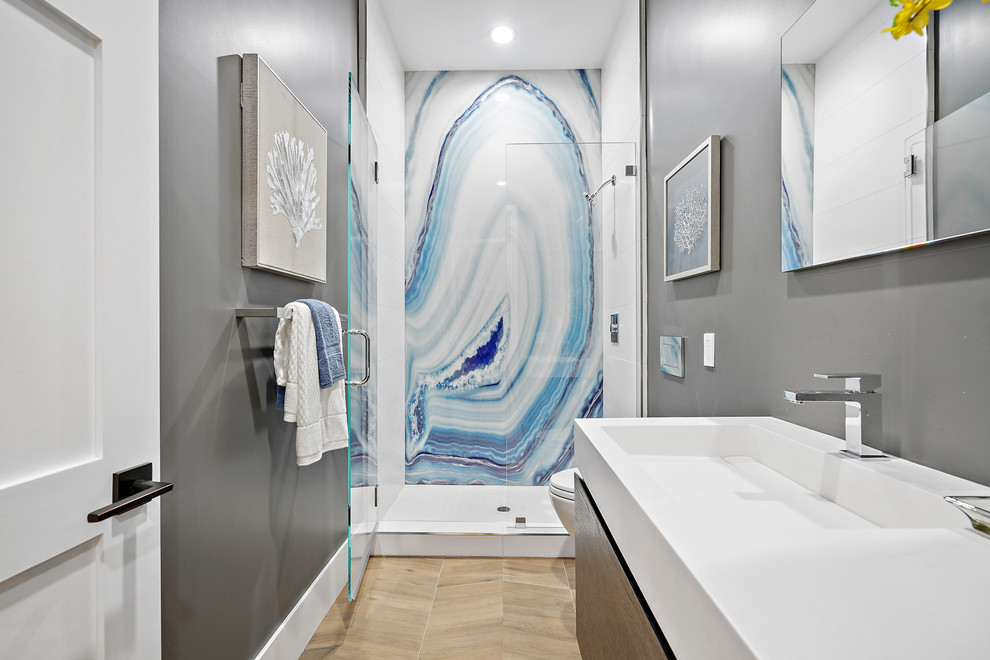 На фото: ванная комната среднего размера в стиле модернизм с плоскими фасадами, фасадами цвета дерева среднего тона, душем в нише, инсталляцией, серыми стенами, светлым паркетным полом, душевой кабиной, монолитной раковиной, столешницей из искусственного кварца, бежевым полом, душем с распашными дверями, белой столешницей, синей плиткой, белой плиткой, плиткой из листового камня, тумбой под одну раковину и подвесной тумбой с