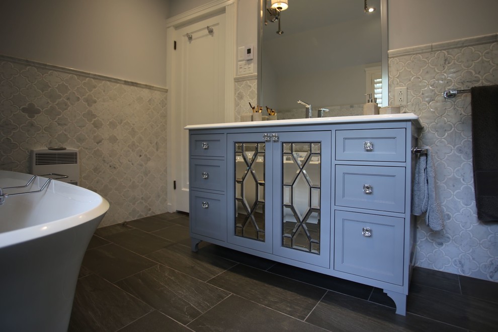 This is an example of a medium sized classic ensuite bathroom in Montreal with glass-front cabinets, grey cabinets, a freestanding bath, a corner shower, a one-piece toilet, grey tiles, marble tiles, grey walls, porcelain flooring, a submerged sink, engineered stone worktops, black floors and a sliding door.