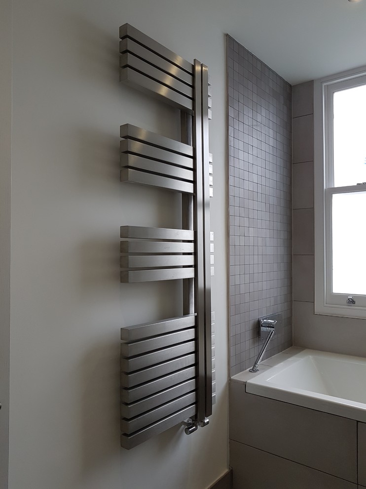 Inspiration for a medium sized contemporary family bathroom in London with medium wood cabinets, a built-in bath, a shower/bath combination, a wall mounted toilet, grey tiles, porcelain tiles, grey walls, porcelain flooring, a wall-mounted sink and tiled worktops.